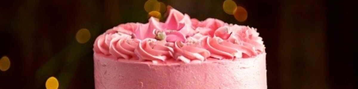 cropped Firefly birthday cake with pink frosting on a white cake stand sitting on a wooden table in a rustic