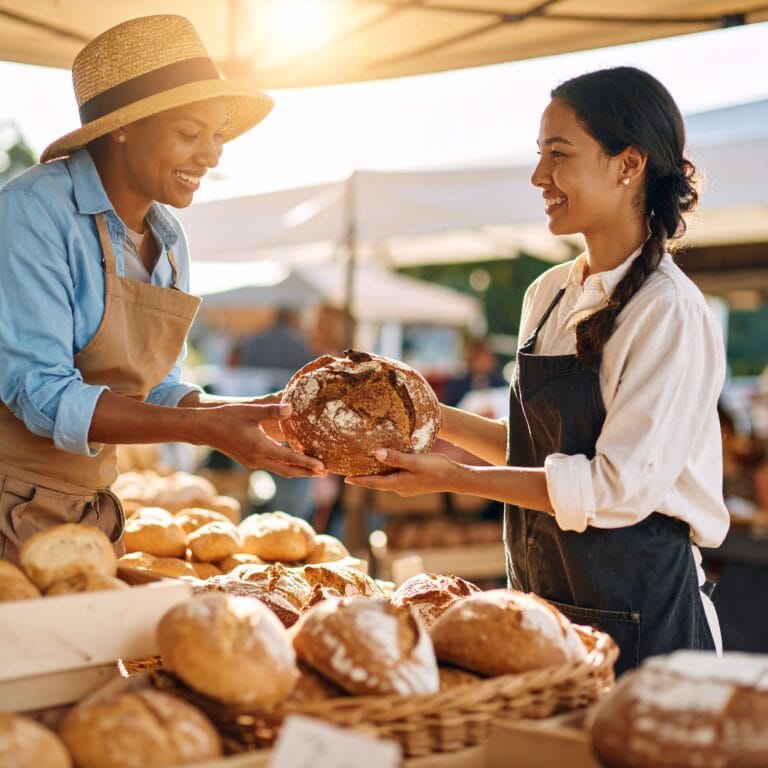 A farmers market vendor selling a loaf of bread to a new customer